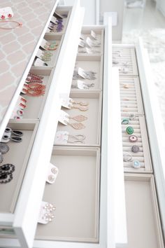 an open drawer with jewelry on it in a white room next to a mirror and wall