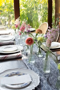 the table is set with plates and flowers in vases on top of it, along with other place settings