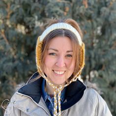 a woman wearing a knitted hat and smiling at the camera with pine trees in the background