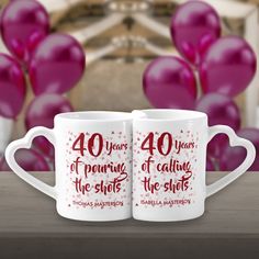 two white coffee mugs sitting on top of a table with balloons in the background