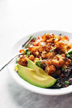 a white bowl filled with meat and veggies next to a fork on top of a table