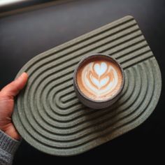 a person holding a cup of coffee on top of a green plate with swirl designs