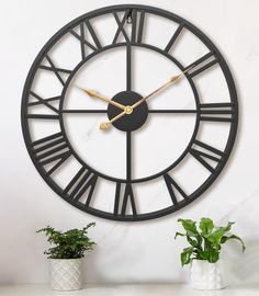 a large black and gold clock sitting on top of a white table next to a potted plant