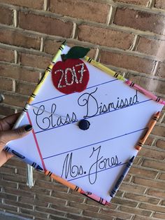 a person holding up a graduation cap with writing on it and an apple attached to the top