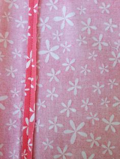 a pink and white flowered fabric with a red ribbon in the center that is being sewn