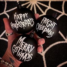 three black ornaments with white writing on them are being held by someone's hand