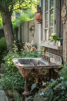 an old rusty sink in front of a window with plants and flowers growing around it