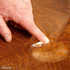 a man's hand pointing at something on a wooden table with brown staining