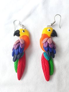 two colorful parrots are hanging from earrings on a white surface, one is painted with multicolored feathers and the other has a black nose