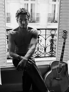 a man sitting on a window sill next to a guitar