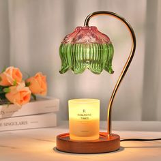 a green glass lamp sitting on top of a wooden table next to a vase filled with flowers