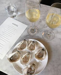 some oysters are on a white plate next to two wine glasses and a menu