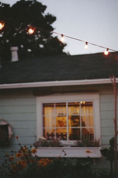 an outside view of a house with lights on the windows and flowers in the foreground