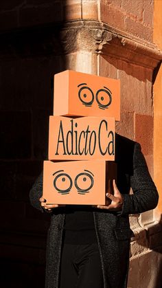 a woman holding two boxes with faces drawn on them and the words adico written on it