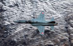 a fighter jet flying through the air over snow covered mountains