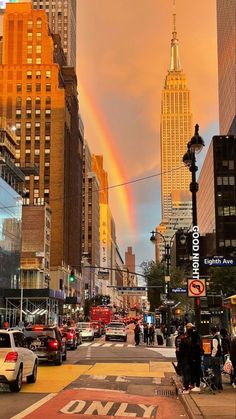 a rainbow in the sky over a city with tall buildings and people walking down the street