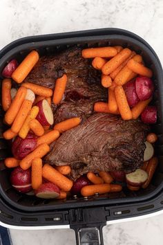 a roaster with carrots, potatoes and meat in it on a marble surface