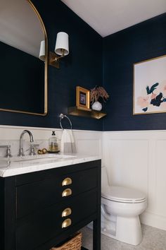 a white toilet sitting next to a sink in a bathroom under a framed painting on the wall