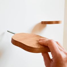 a person holding a piece of wood with nails stuck to the top of it, in front of a white wall