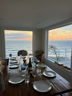 a dining room table with plates and wine glasses on it in front of a large window overlooking the ocean