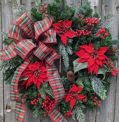 a wreath with poinsettis and pine cones is hung on a wooden fence