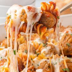 a spoon full of pasta and meatballs being lifted from a casserole dish