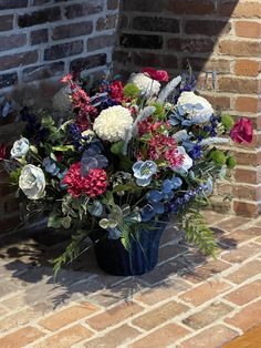 a blue vase filled with lots of flowers on top of a brick floor next to a wall