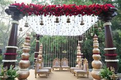 an outdoor wedding ceremony setup with red roses and hanging bells on the ceiling, decorated in gold