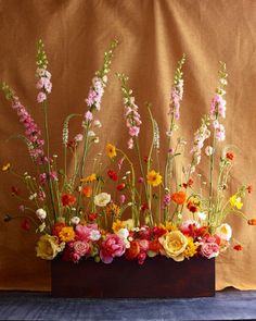 a vase filled with lots of colorful flowers on top of a wooden table next to a brown wall