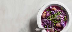 a white bowl filled with purple cabbage and peas next to a spoon on top of a table