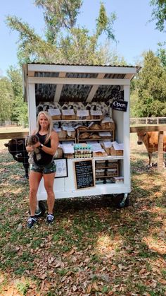 a woman standing in front of a kiosk holding a small dog and smiling at the camera