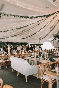 tables and chairs are set up in a tent with greenery hanging from the ceiling