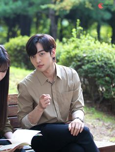 two people sitting on a bench in the park, one reading a book and the other writing