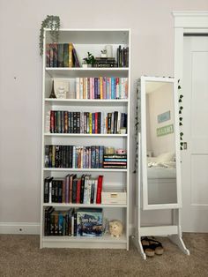 a white book shelf sitting next to a mirror on top of a carpeted floor