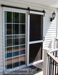 an open sliding glass door on the outside of a house with white siding and black shutters