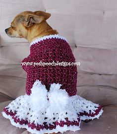 a dog wearing a red and white dress on top of a couch next to a pillow