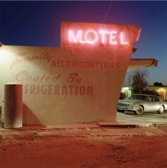 an old motel sign is lit up at night with cars parked in the parking lot