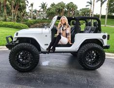 a white jeep with black wheels parked in a parking lot next to palm trees and water