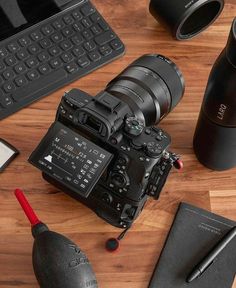 a camera sitting on top of a wooden table next to a keyboard and cup with a pen