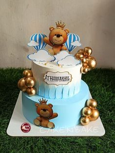 a teddy bear on top of a blue and white cake with gold balloons around it