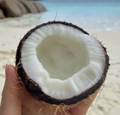 a person holding up a half eaten coconut on the beach