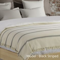 an unmade bed with white linens and striped blankets on it, in front of a brick wall