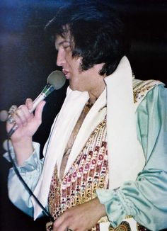 elvis presley singing into a microphone while wearing a white scarf and green shirt with gold accents