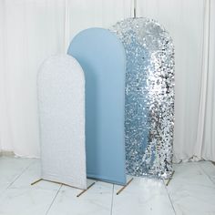 two large silver and blue decorative objects on white tiled floor next to curtained window