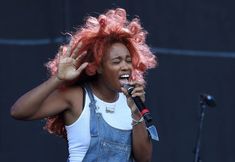 a woman with red hair singing into a microphone and holding her hands up in the air