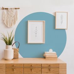 a blue circle painted on the wall next to a wooden dresser with two pictures and a potted plant