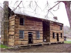 an old log cabin sits in the middle of a field with no grass and bare trees