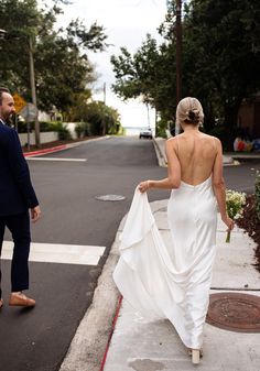 a woman in a white dress is walking down the street with her back to the camera