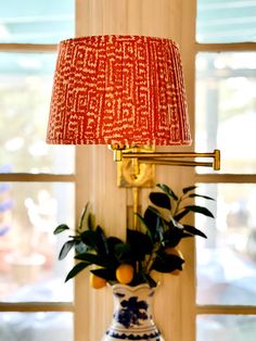 a blue and white vase with a red lamp on it next to a large window