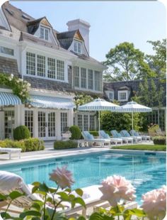 an outdoor swimming pool surrounded by lawn chairs and umbrellas in front of a large white house